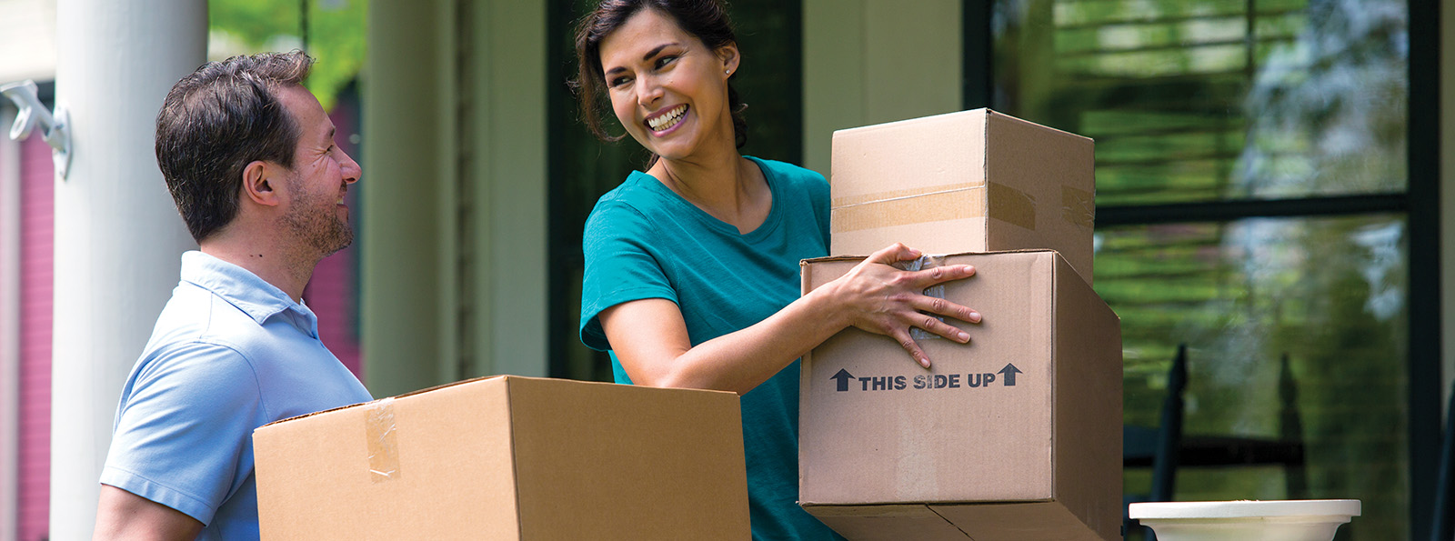 a couple smiles and carries moving boxes into a new home