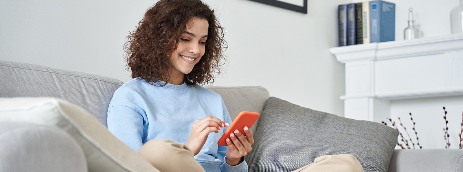 A young woman sitting on the couch using a mobile device for online banking and smiling