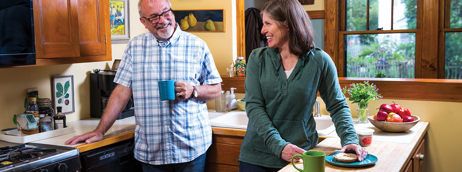 an older couple smiles at each other in their kitchen as they breakfast and coffee ready