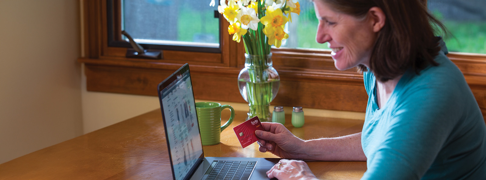 woman smiling and holding a Sovita credit card while shopping online on a laptop