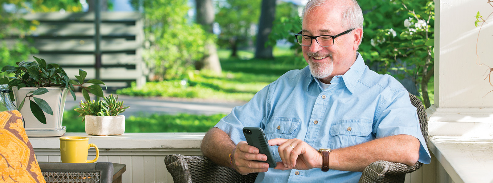 an older man sitting outside on a porch using his phone for mobile banking