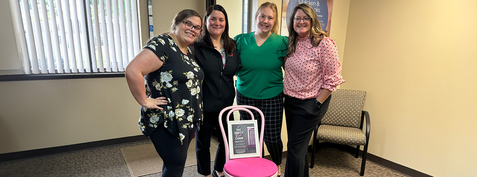 Four women pose behind the Empty Pink Chair