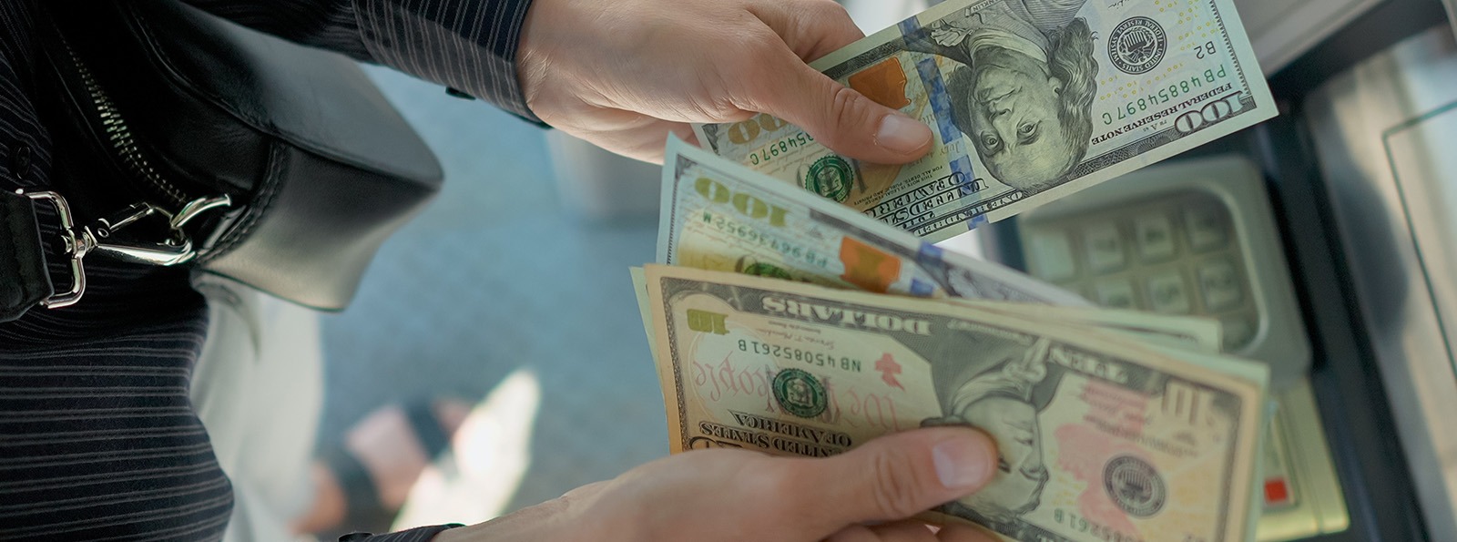 An overhead photo of a person holding several large denomination US bills in front of a Sovita ATM