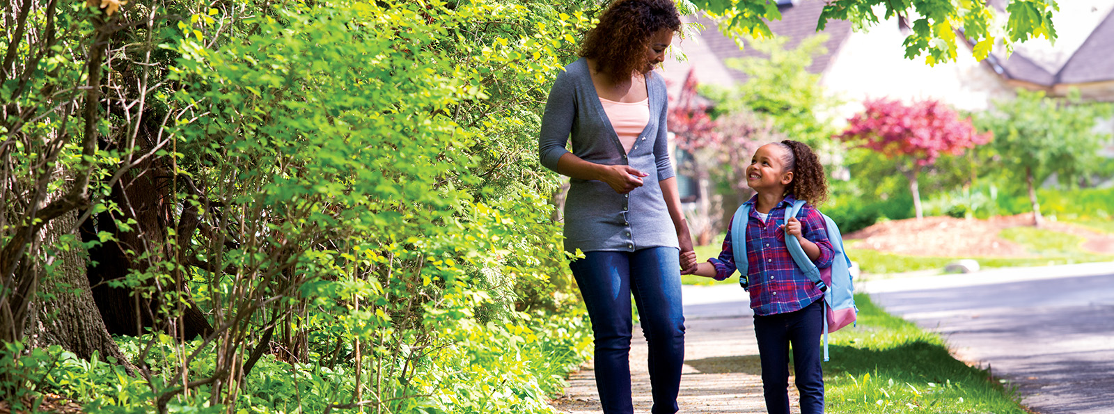 a mother and daughter hold hands while they walk to school on a sunny day