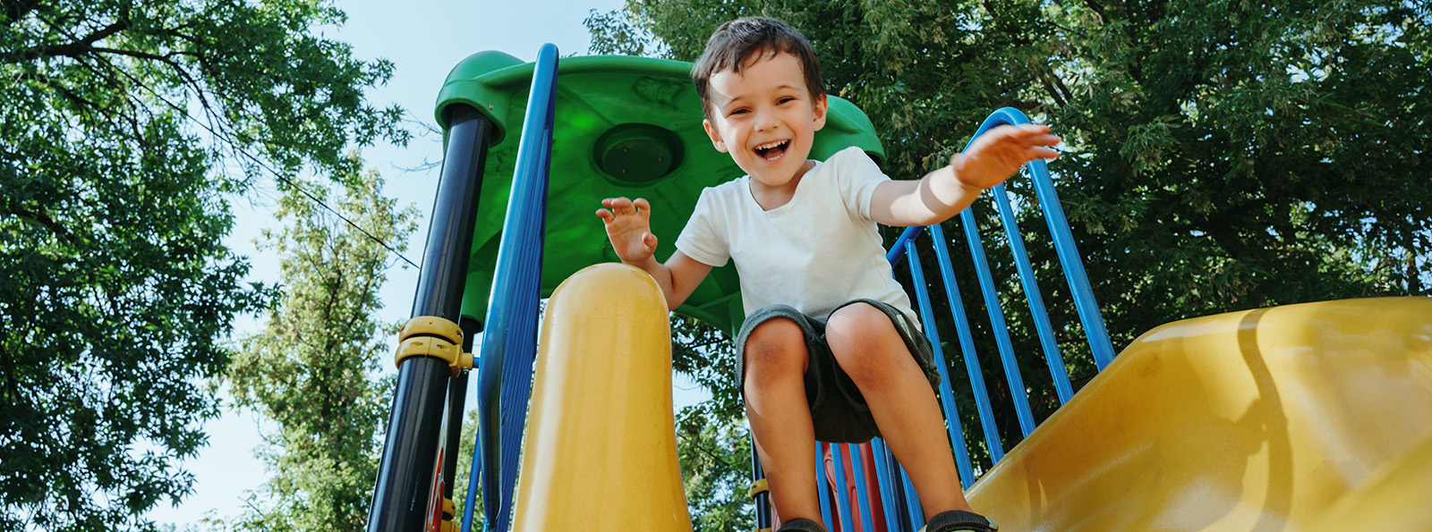 a smiling young boy at the top of a slide ready to slide down