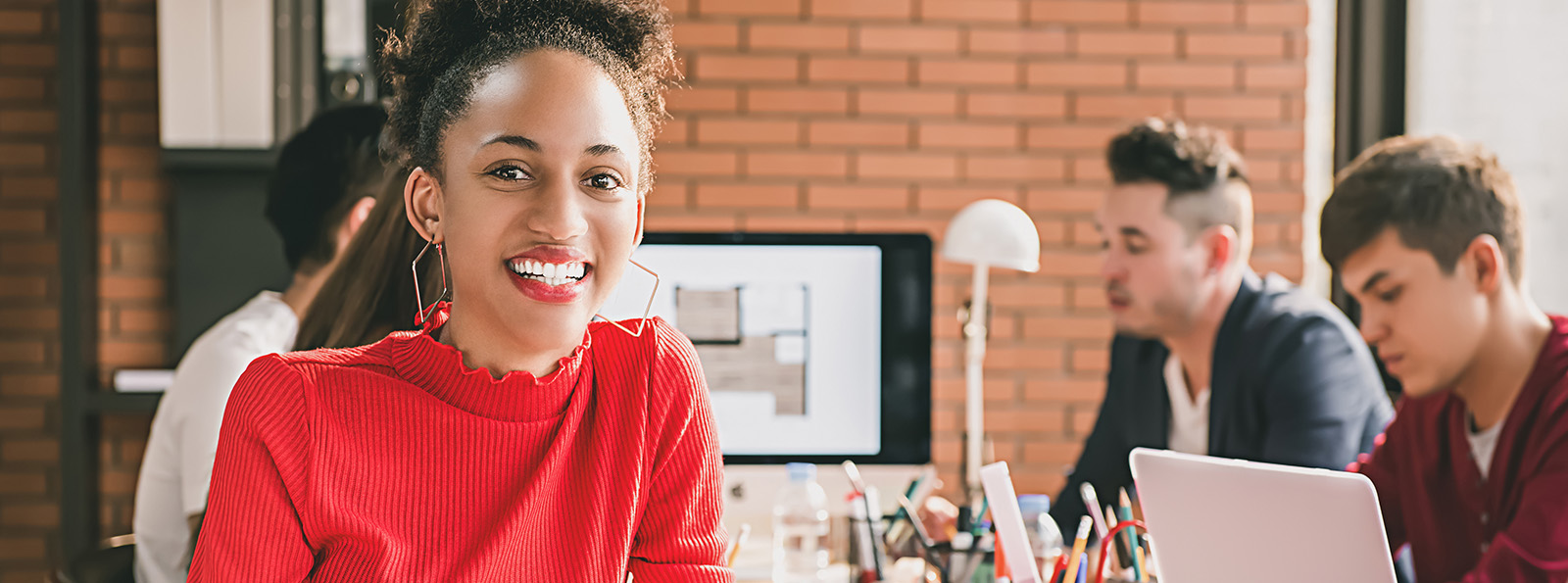 a young professional woman smiling at a table with other young professionals working