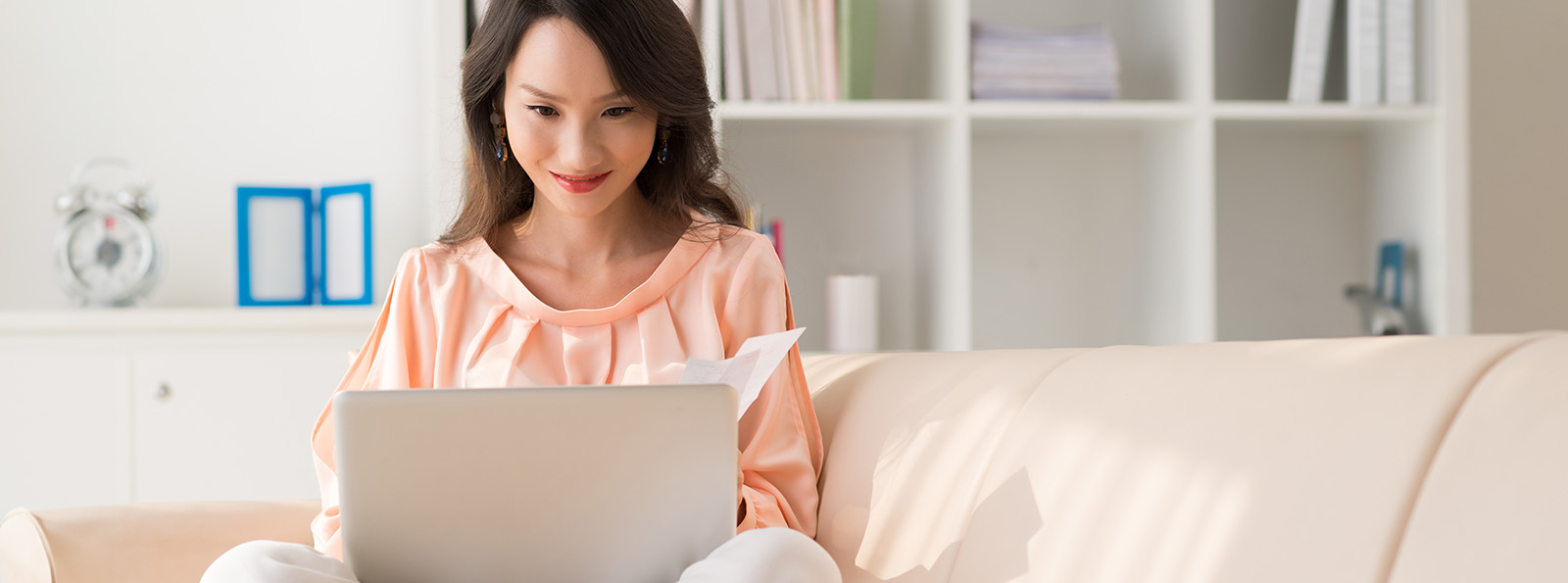 a smiling woman sits on her couch and works on her laptop